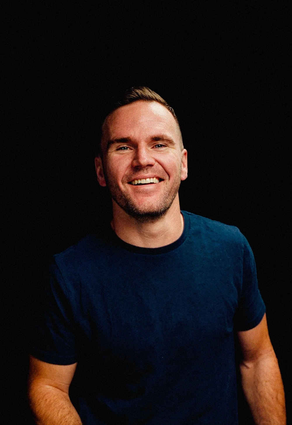 Brad Hussey, smiling, in a navy t-shirt on a black background.