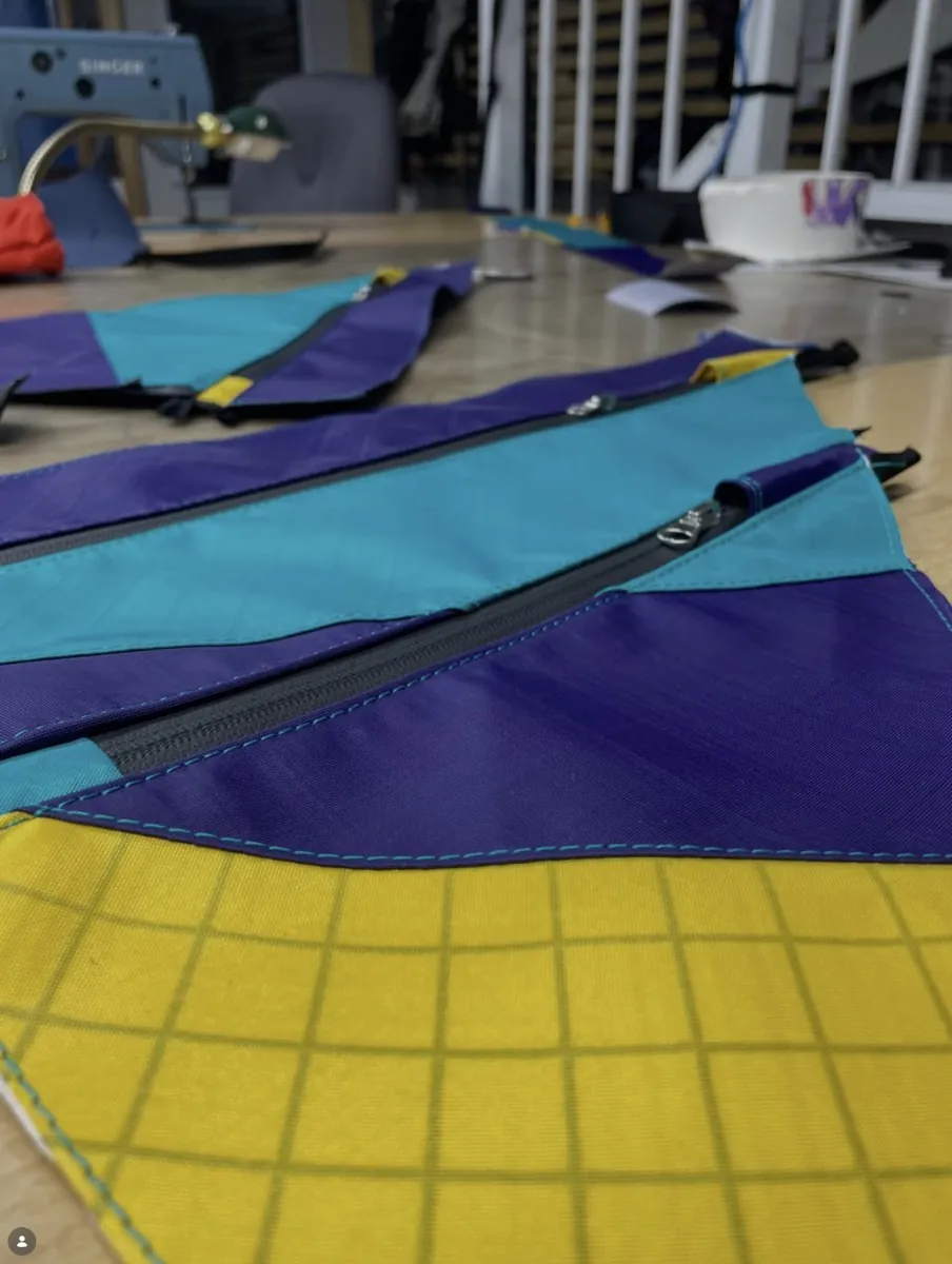 A frame bag in teal, purple and yellow panels on the workshop table